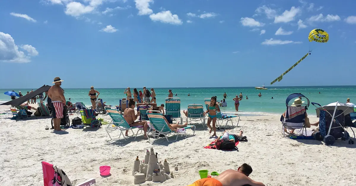 Beach chairs on white sand with turquoise water and a parasail overhead