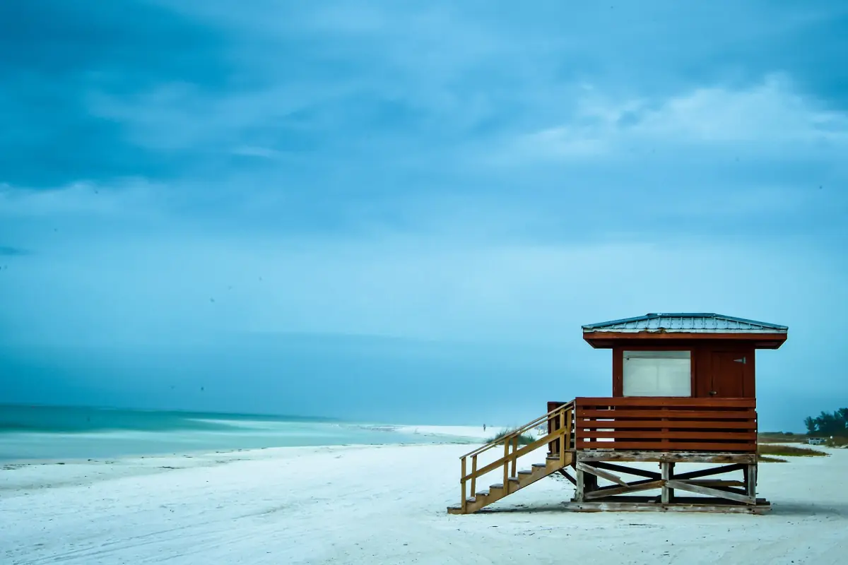 Brown lifeguard tower on white sand beside turquoise water at Lido Beach