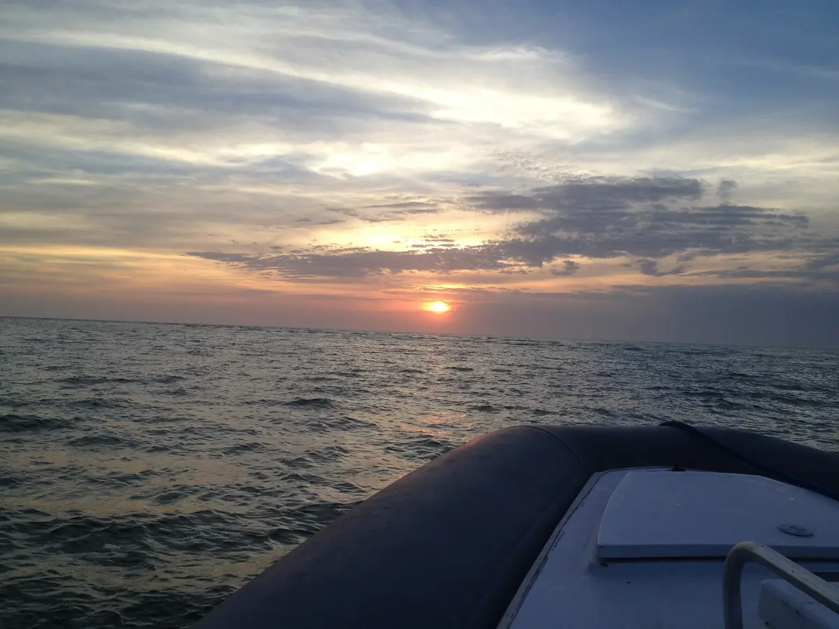 Bow of a boat gliding over the water toward a cloudy sunset