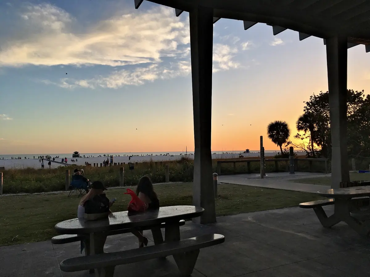 Picnic tables under a beach shelter with a glowing sunset behind