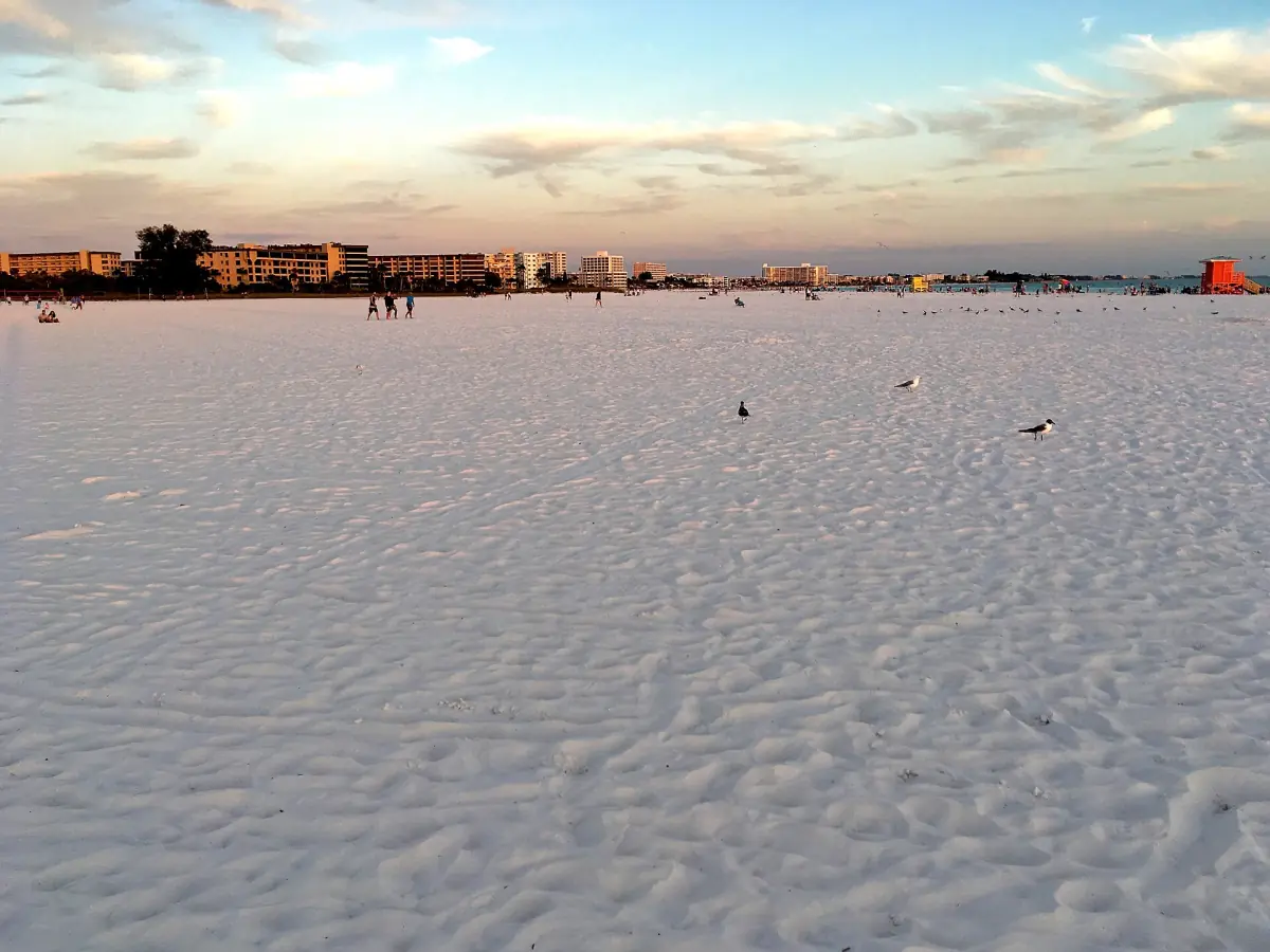 Endless flat white sand with beachfront buildings in the distance at sunset