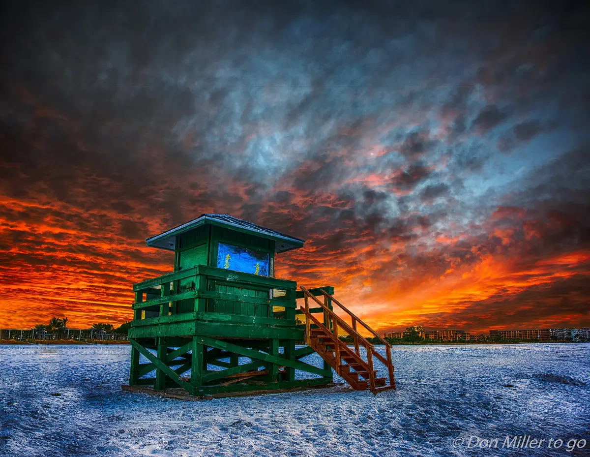 Green lifeguard stand beneath a dramatic orange and blue morning sky