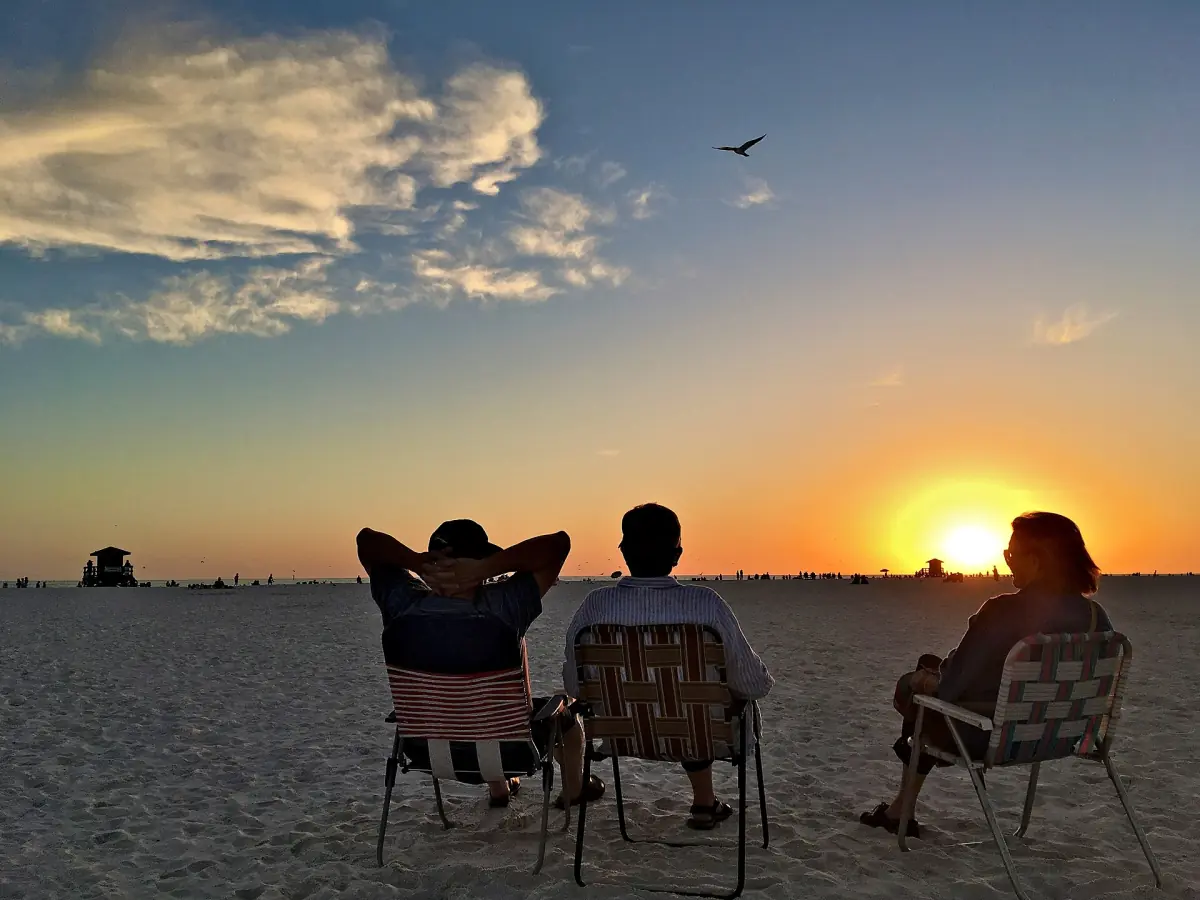 Sun touching the horizon while beachgoers sit in chairs on the sand