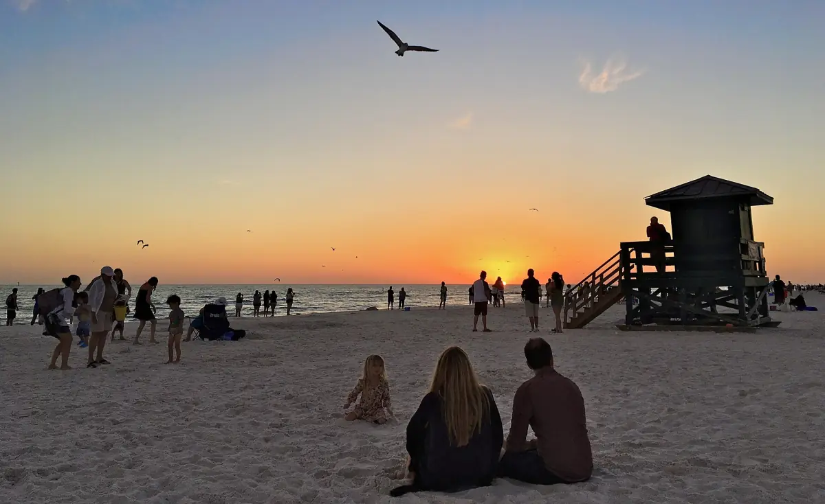 Visitors gather on the sand at sunset beside a dark lifeguard tower